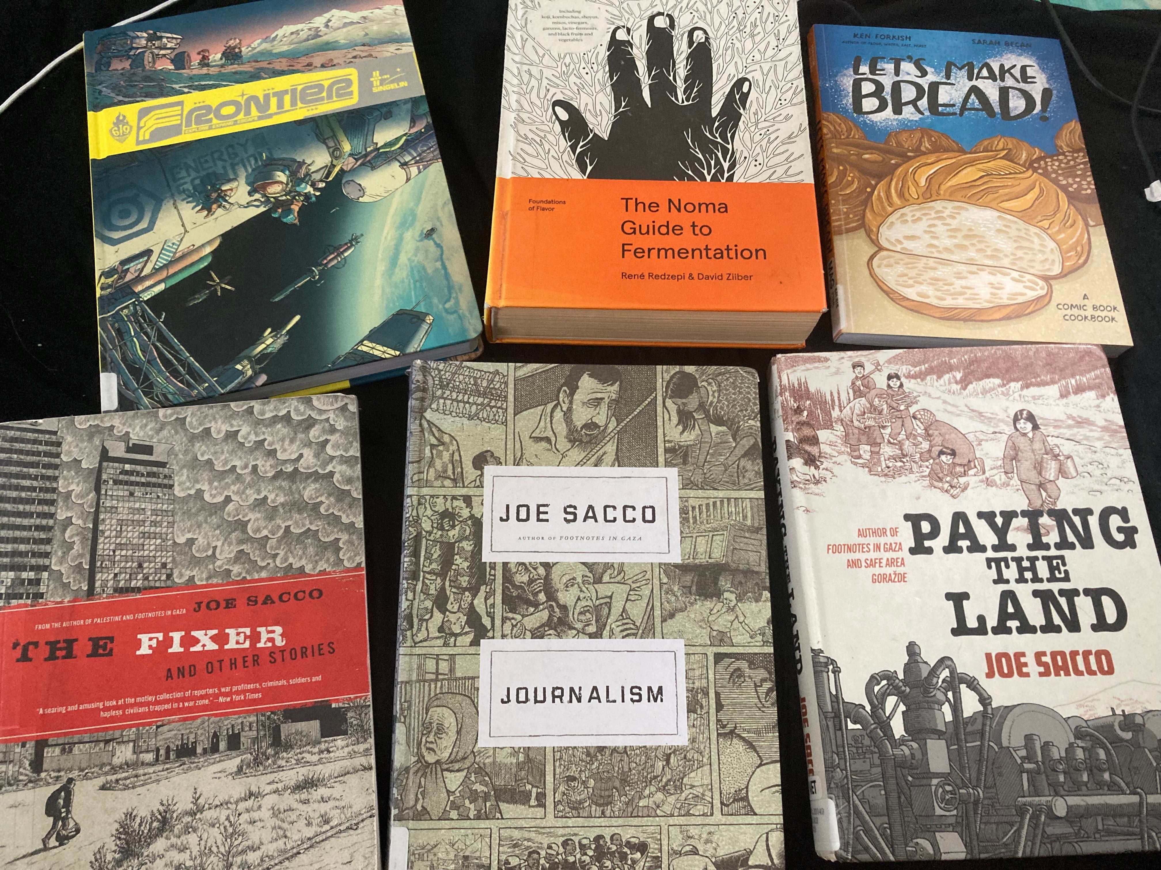 clockwise from top left: singelin’s Frontier, The Noma Guide to Fermentation, Let’s Make Bread, Sacco’s Paying the Land, Journalism, and The Fixer and other stories